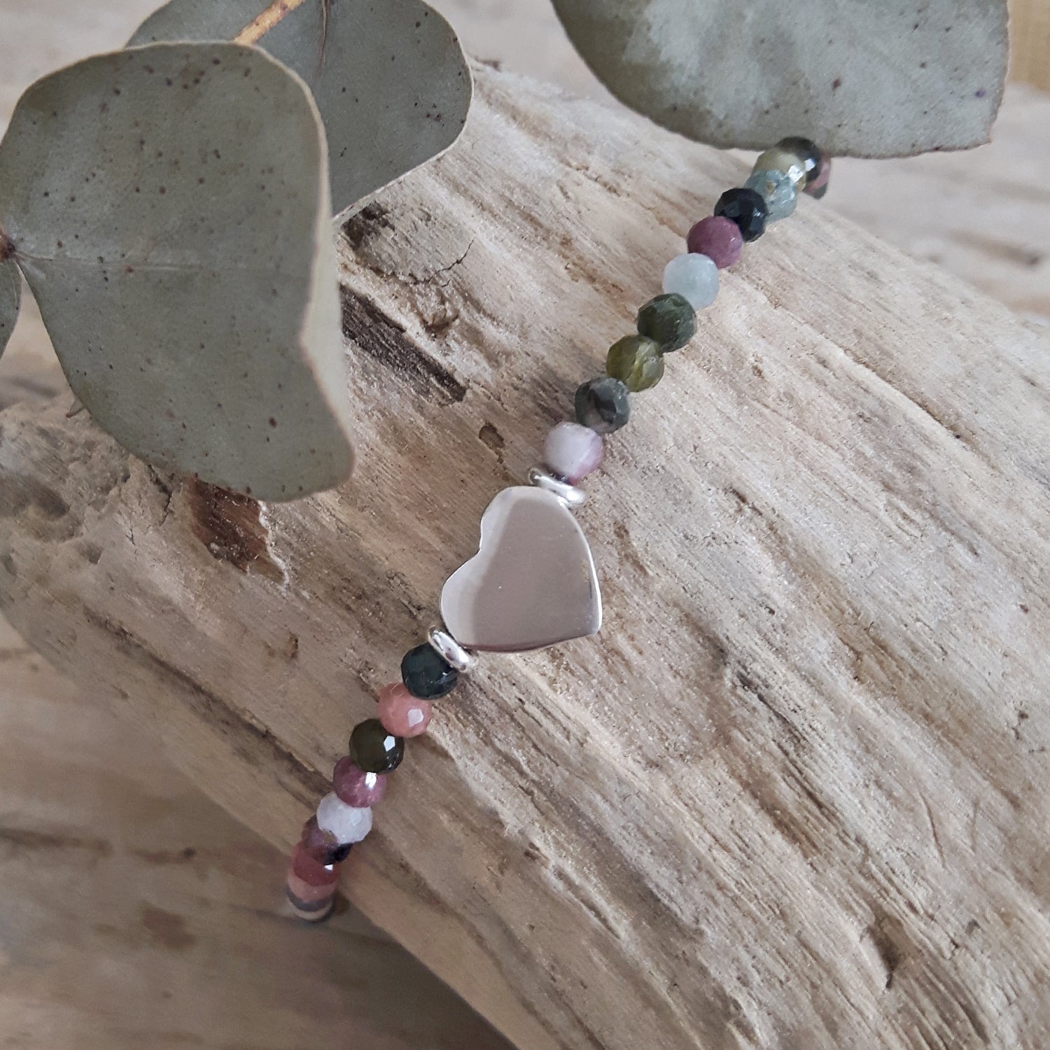 Tourmaline beaded bracelet with a sterling silver heart charm on a wooden surface
