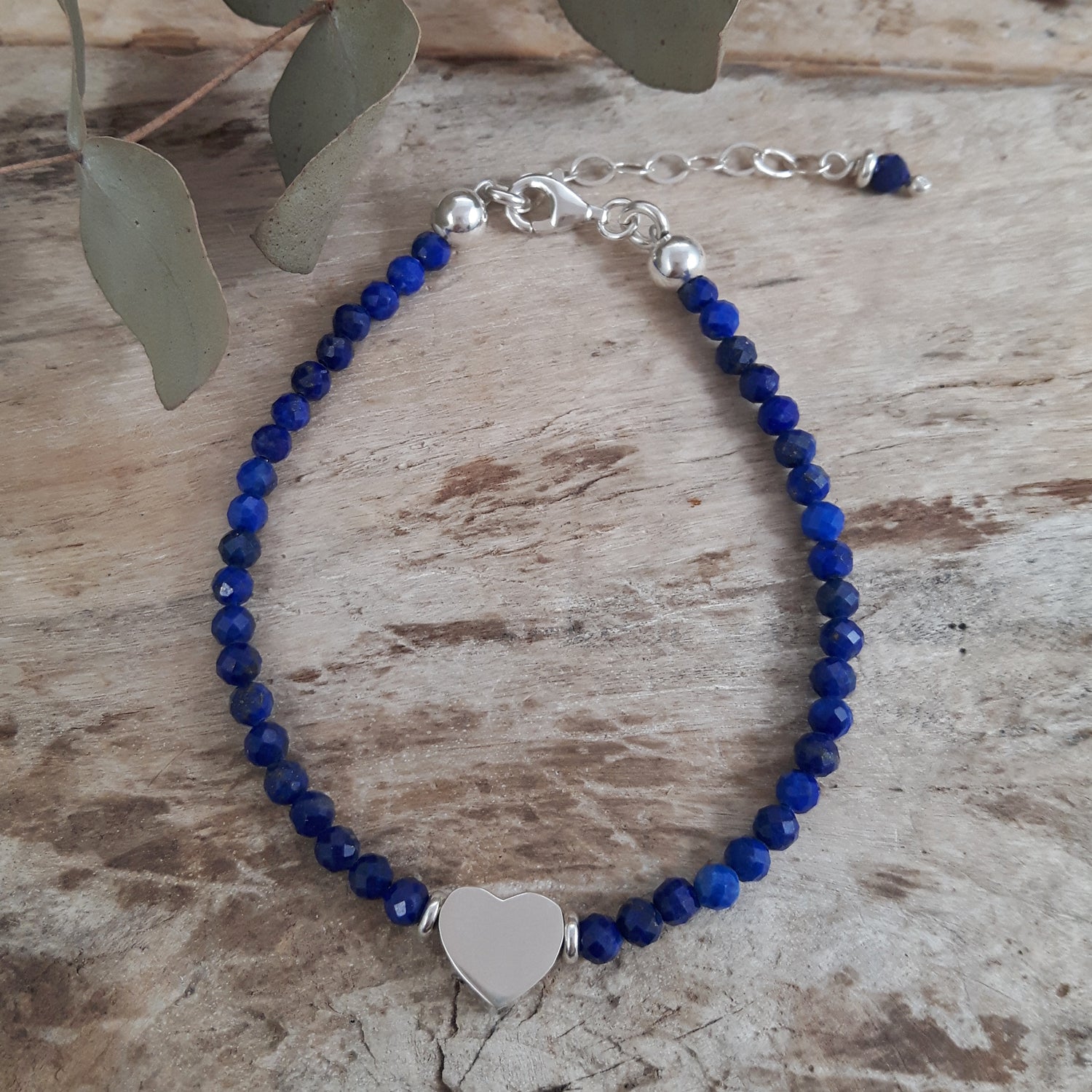 Handmade blue lapis gemstone beaded bracelet with a sterling silver heart charm on a wooden surface