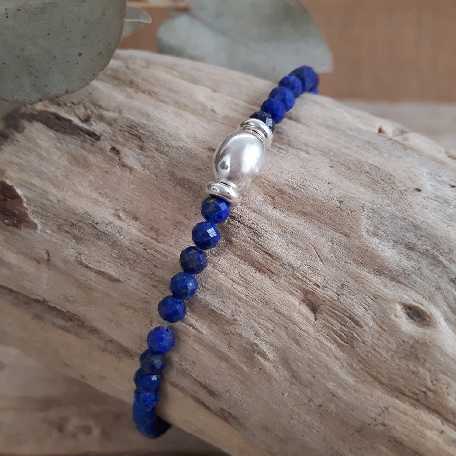 Blue lapis gemstone beaded bracelet with a sterling silver bead on a wooden surface