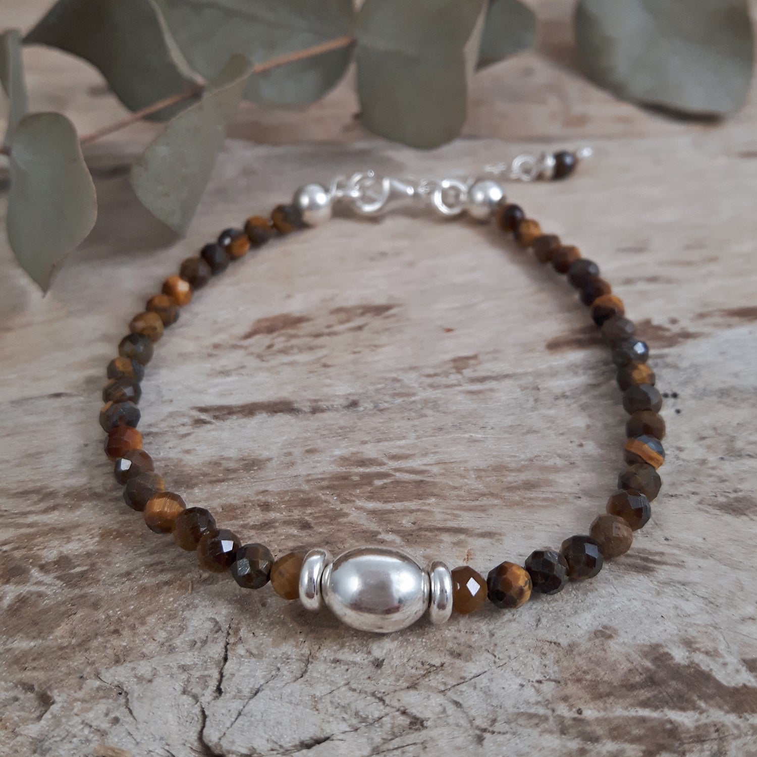 Tiger's eye beaded bracelet with sterling silver accents on a wooden surface with leaves in the background