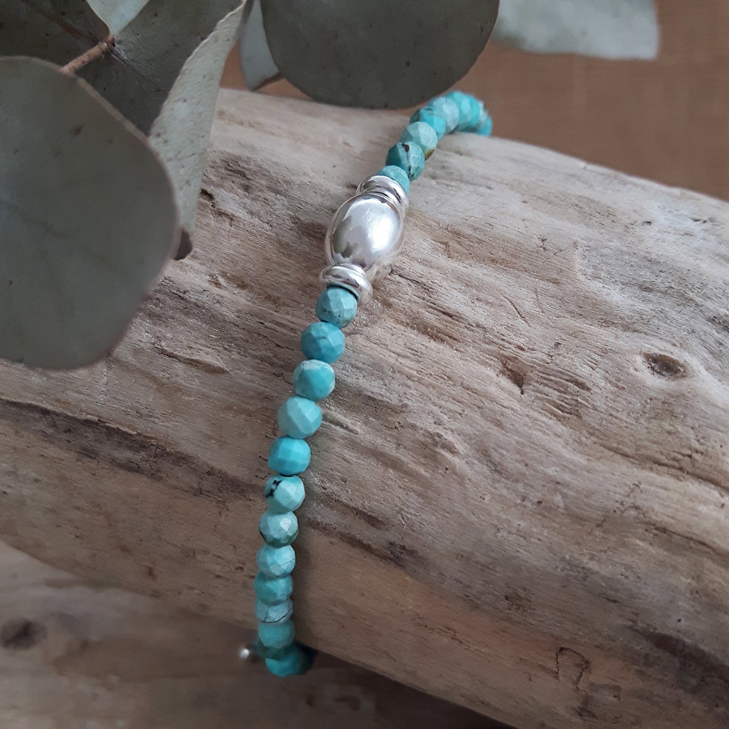 Turquoise beaded birthstone bracelet with a sterling silver central bead on a wooden surface