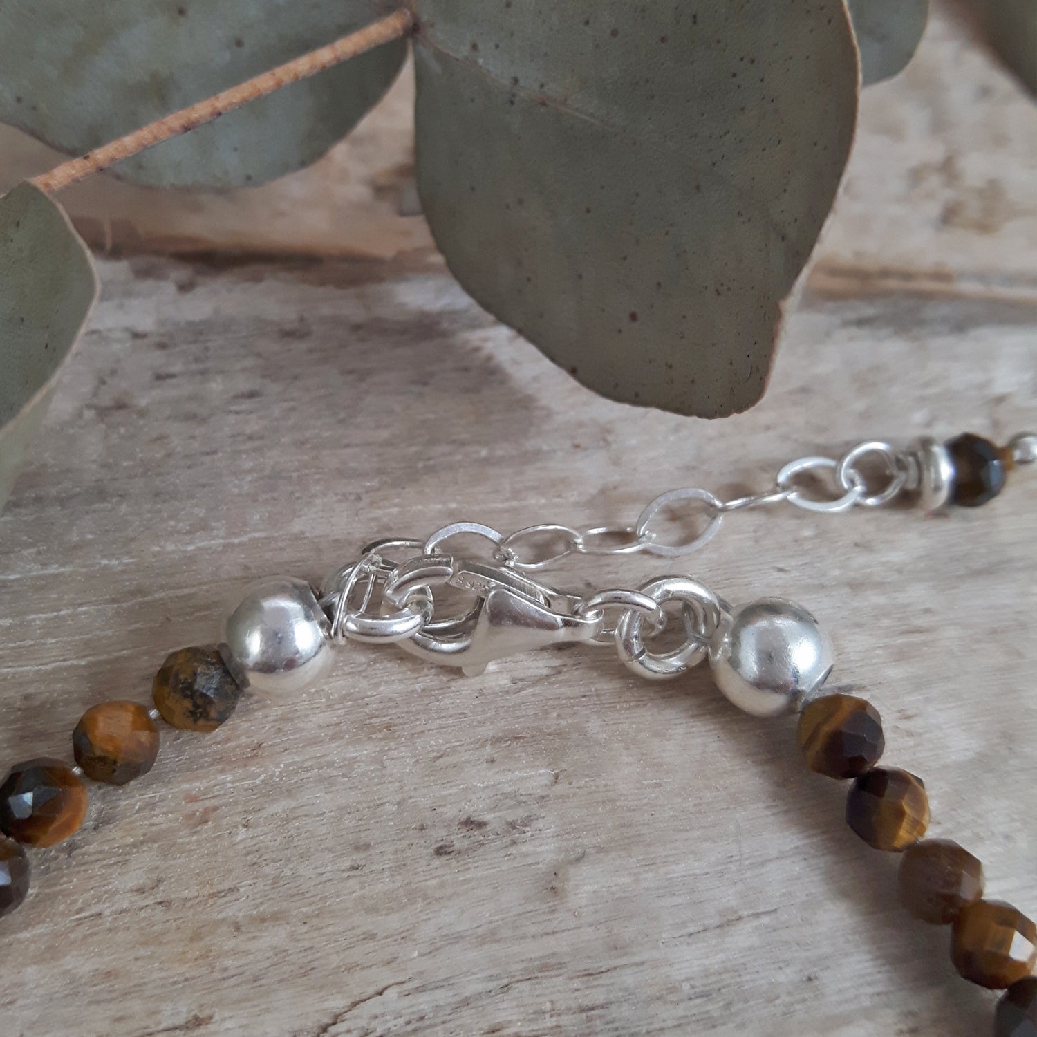 Sterling silver extender chain and brown  tiger's eye beaded necklace on a wooden surface with leaves in the background