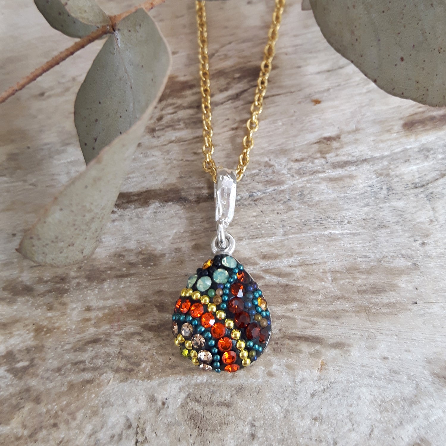 Gold-plated Chain Necklace with a colourful teardrop pendant on a wooden surface. Multi-coloured micro-pearls and crystals hand-set in sterling silver.