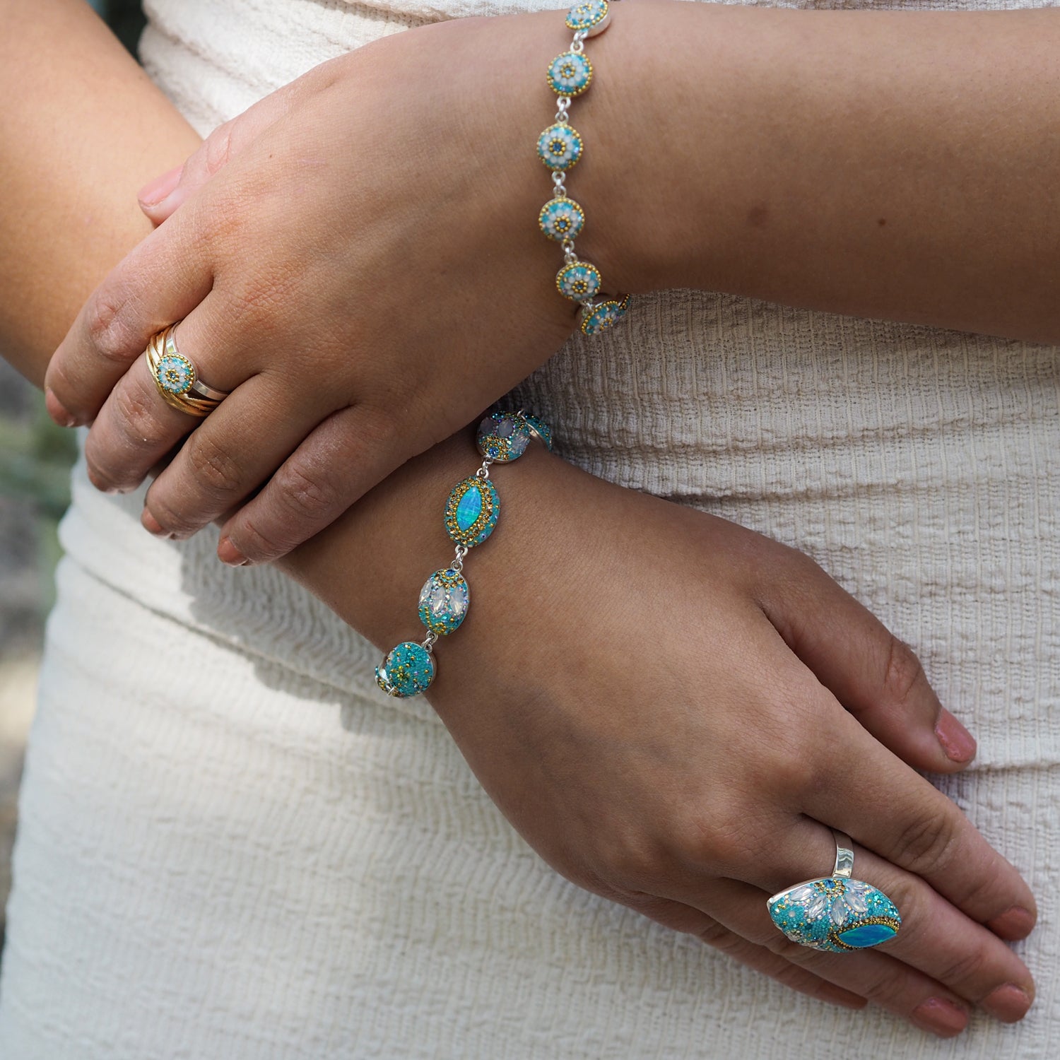 Close-up of hands wearing turquoise jewellery on a neutral background