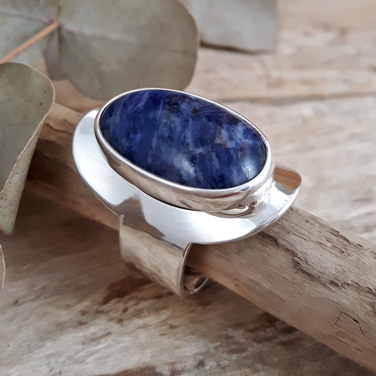 Sterling silver ring with a hand-set blue sodalite gemstone on a wooden surface with leaves