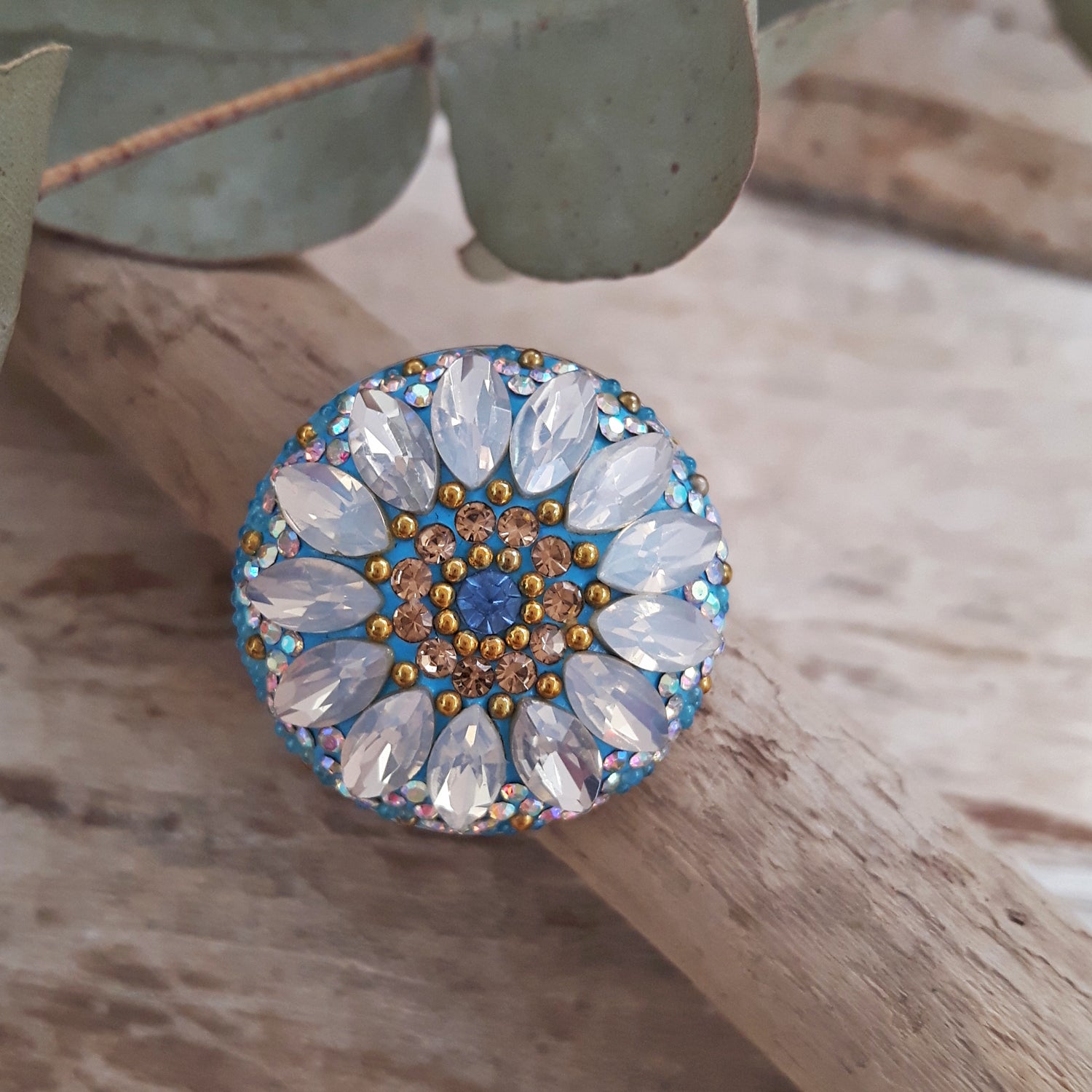 An adjustable sterling silver ring with a daisy motif adorned with clear crystal petals and a mix of turquoise, aqua, and clear crystals, displayed on a wooden surface.