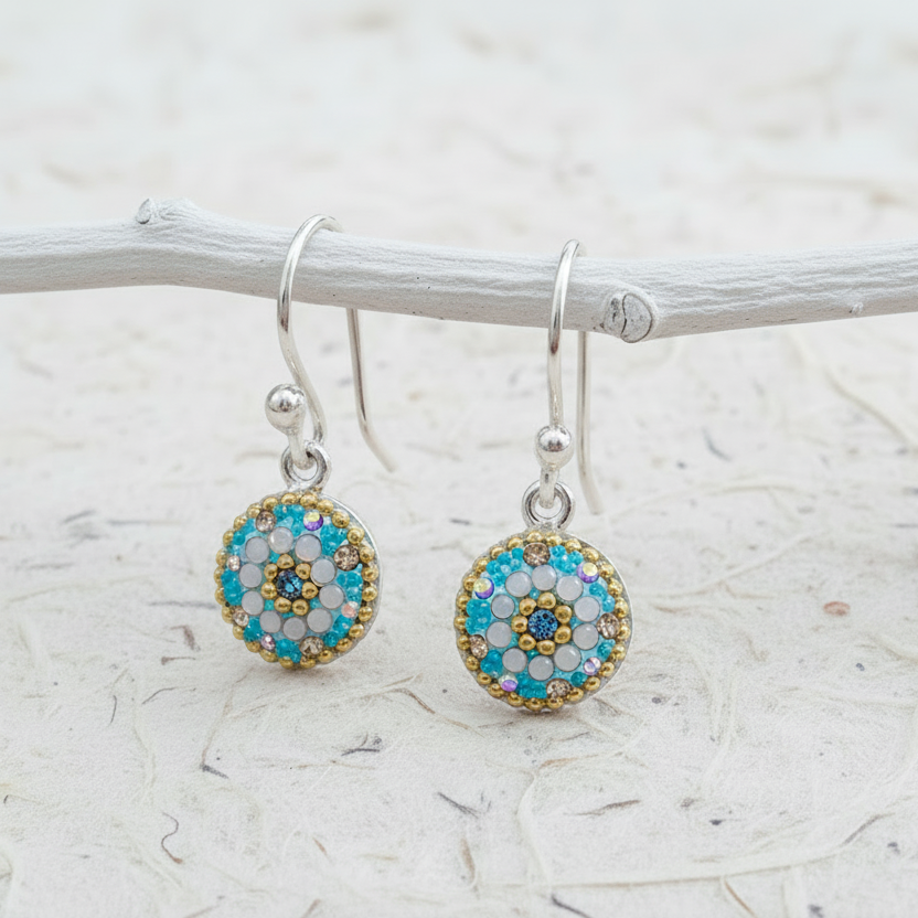 Pair of round earrings with blue and gold details on a white branch background