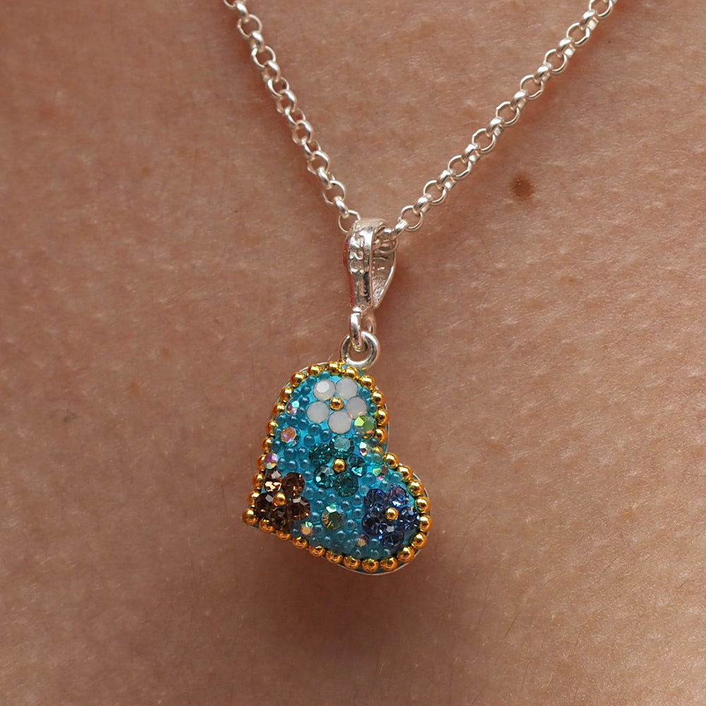 A sterling silver heart-shaped pendant with micro-crystals and color tones of turquoise, aqua, and gold, displayed on a chain.
