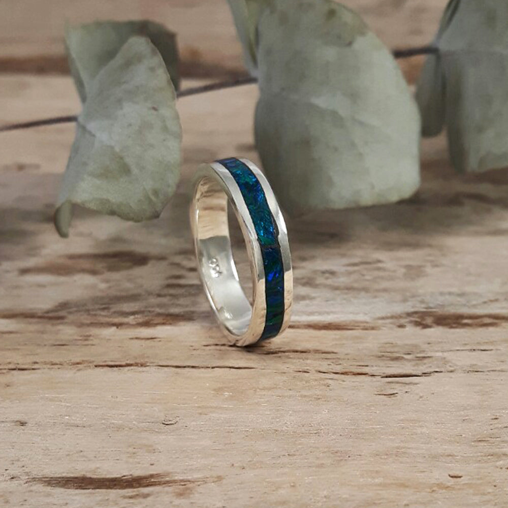 A Flinder Emerald Opal ring with a ribbon of emerald green opal nestled between two bands of sterling silver, displayed on a wooden surface.